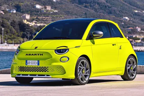 Jaskrawożółty Abarth 500 EV z czarnym dachem stoi na tle wzgórz i morza.