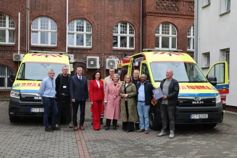 Grupa osób pozuje przed dwoma ambulansami. Jeden z mężczyzn trzyma dokument, być może związany z czn rejestracja.