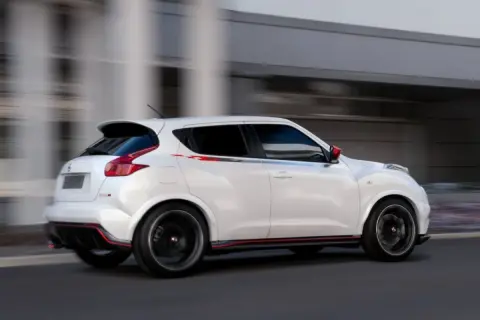 Biały Nissan Juke 1.5 dCi w wersji Nismo, z czerwonymi akcentami, pędzi ulicą. Jego sportowy wygląd budzi pozytywne opinie.
