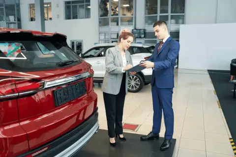 Kobieta podpisuje dokumenty przy nowej, czerwonej Toyocie. To jej pierwszy przegląd gwarancyjny.