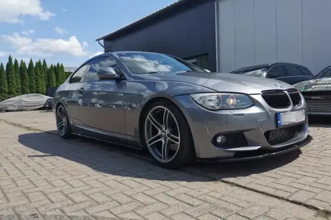 Szare BMW E92 335d z przyciemnianymi szybami i sportowym dyfuzorem, zaparkowane na zewnątrz.