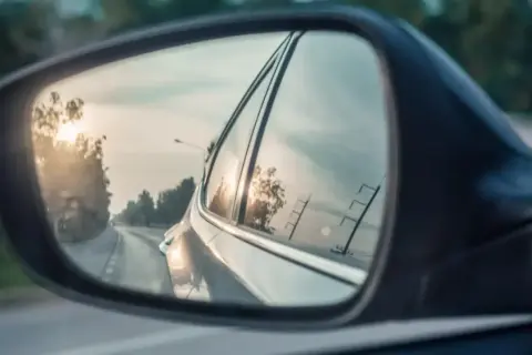 Widok z lusterka bocznego Toyoty. Słońce odbija się w szybie, a droga wije się w oddali.