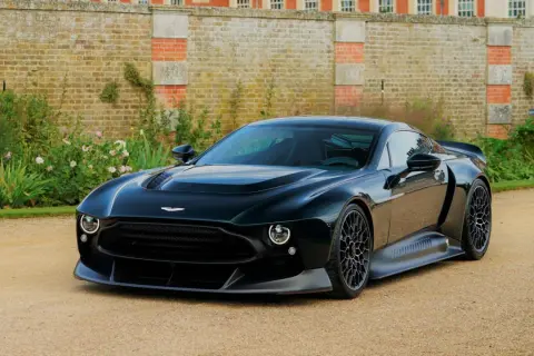Elegancki, czarny Aston Martin Victor prezentuje się majestatycznie na tle zabytkowego dworu i bujnej zieleni.