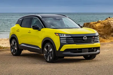 Żółty Nissan Kicks z czarnym dachem stoi na plaży przy spokojnym morzu.