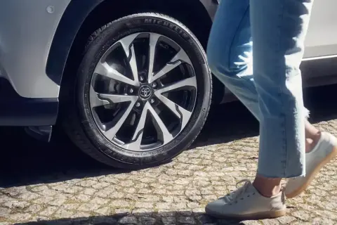 Osoba w jeansach i białych butach zbliża się do Toyoty Corolli. Dowiedz się, jak zresetować czujnik ciśnienia w oponach.