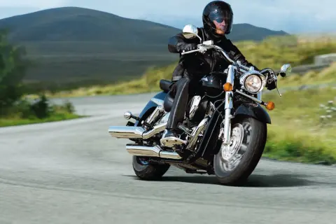Mężczyzna w kasku i skórzanej kurtce jedzie na motocyklu Honda VTX 1800. Wady i zalety tego potężnego cruisera są dyskutowane podczas jazdy po malowniczej drodze.