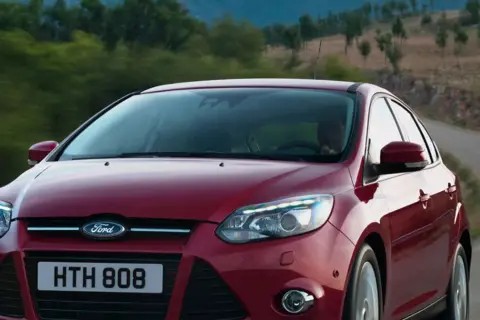 Czerwony Ford Focus 2011 na krętej drodze wśród zieleni.