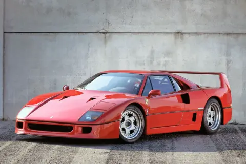 Ikoniczny czerwony Ferrari F40 z charakterystycznym skrzydłem, zaparkowany na tle betonowej ściany.