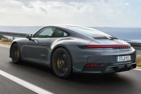 Szary Porsche 911 GTS pędzi po krętej drodze z widokiem na morze.
