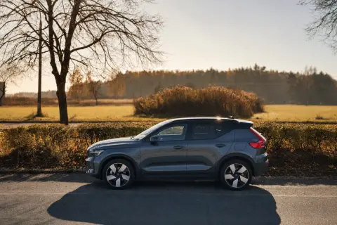 Szary Volvo EX40 zaparkowany na poboczu drogi, w tle jesienny krajobraz z drzewami i krzewami.