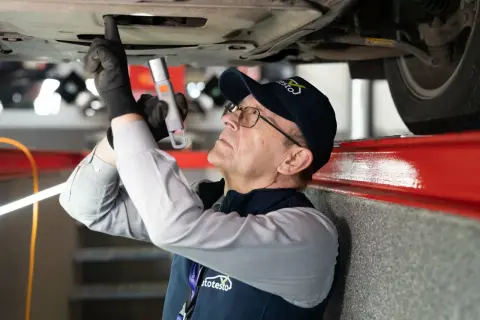 Mechanik w czapce z logo "autotesto.pl" sprawdza podwozie auta, szukając usterek. To kluczowe dla rankingu najlepszych firm od sprawdzania auta przed zakupem.