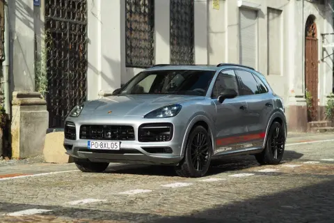 Srebrny Porsche Cayenne GTS z czerwonymi akcentami na progach, zaparkowany na brukowanej ulicy przed zabytkową kamienicą.