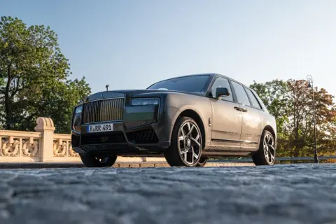 Elegancki Rolls-Royce Cullinan na kamienistej drodze, z grillem i charakterystyczną figurką na masce.