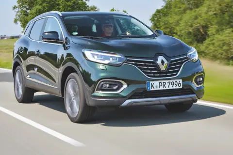 Zielony Renault Kadjar jedzie po drodze, za kierownicą mężczyzna w okularach.