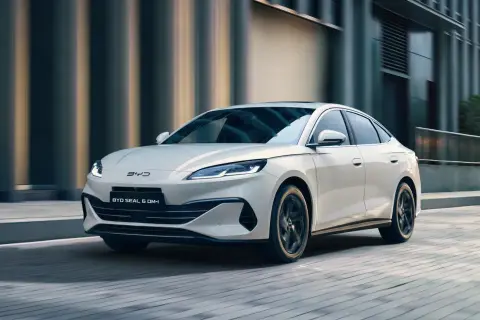 Biały BYD Seal 6 DM-i sunie ulicą, otoczony miejską architekturą i zielenią.