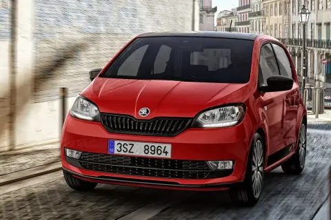 Czerwony Skoda Citigo z czarnym dachem pędzi ulicą miasta.