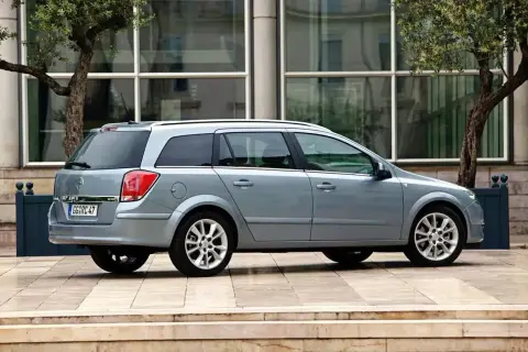 Srebrny Opel Astra H kombi stoi przed nowoczesnym budynkiem.