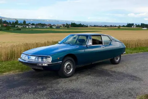 Piękny, turkusowy Citroen SM na tle złotego pola i jeziora. Klasyk motoryzacji w malowniczej scenerii.