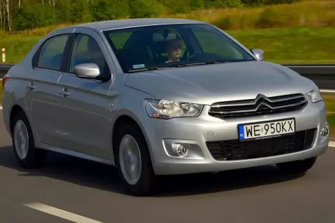 Srebrny Citroen C Elysee jedzie po drodze, za kierownicą siedzi mężczyzna.