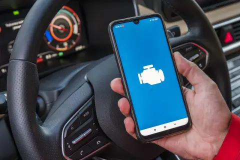 Ręka trzyma smartfon z ikoną silnika, gotowy do diagnostyki Toyoty. Jaki program do Toyoty z ELM327?