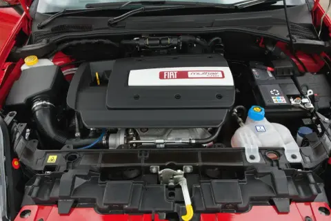 Silnik MultiAir Turbo w Fiat Grande Punto 1.4. Widoczny jest czarny plastikowy dekiel z logo Fiata, akumulator i zbiornik płynu chłodniczego.
