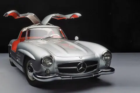 Srebrny Mercedes 300SL z otwieranymi do góry drzwiami, z czerwonym wnętrzem, prezentuje się elegancko na ciemnym tle.