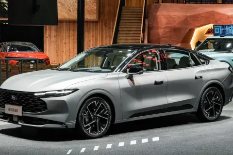 Nowy Ford Mondeo MK2 w kolorze srebrnym, z czarnym dachem, prezentuje się elegancko na tle innych samochodów i drewnianych elementów wystroju.