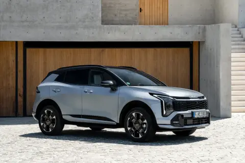 Srebrny Kia Sportage GT Line z czarnym dachem zaparkowany przed nowoczesnym budynkiem z drewnianymi drzwiami i betonowymi schodami.