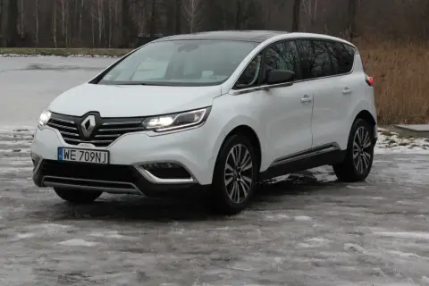 Biały Renault Initiale na oblodzonym podjeździe, z widokiem na zamarznięte jezioro i drzewa.