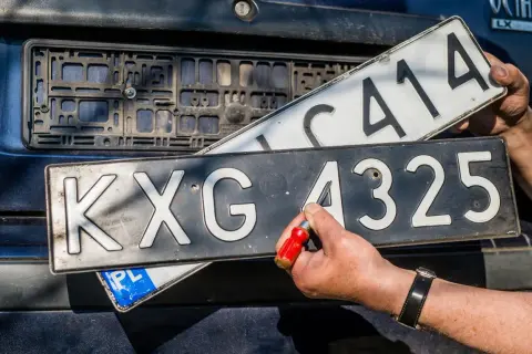 Ręce wymieniają tablice rejestracyjne. Jedna z nich, z numerem KXG 4325, jest przykręcana. To ważny etap w procesie rjs rejestracja.