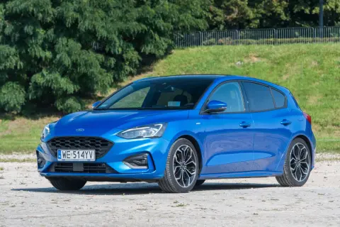 Niebieski Ford Focus 1.0 EcoBoost z czarnym dachem, zaparkowany na żwirowej nawierzchni, na tle zieleni.