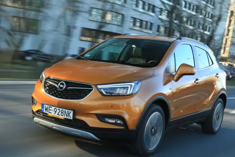 Pomarańczowy Opel Mokka 2015 pędzi ulicą, odbijając światła miasta w swojej lśniącej karoserii.