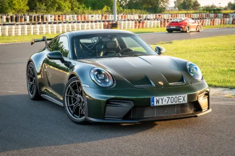 Zielony Porsche 911 GT3 na torze wyścigowym, z innym czerwonym samochodem w tle.