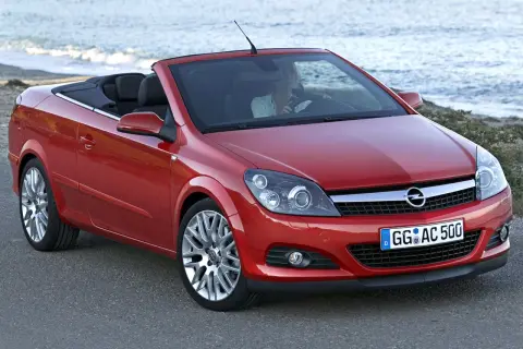 Czerwony opel cabrio z opuszczonym dachem, zaparkowany przy plaży. Kobieta za kierownicą cieszy się jazdą.