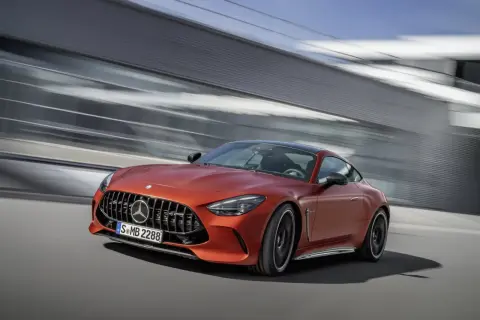 Pomarańczowy Mercedes-AMG GT 63 S pędzi obok nowoczesnej architektury.