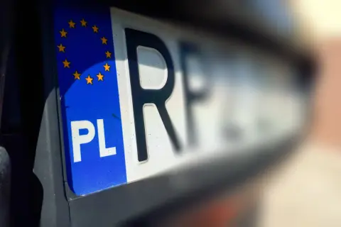 Zbliżenie na polską tablicę rejestracyjną z symbolem UE. Litery "PL" i fragment kolejnych liter są wyraźne, reszta tablicy rozmyta.