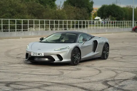 Srebrny McLaren GT z czarnym dachem, zaparkowany na placu z widocznymi śladami opon.