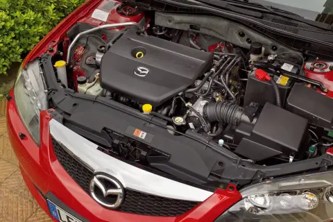 Silnik Mazdy 6 GG, czarny plastikowy kolektor dolotowy z logo Mazda, akumulator i elementy układu chłodzenia.