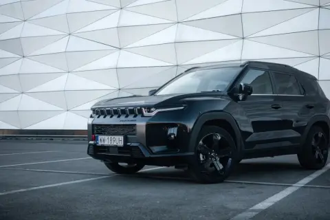Czarny SsangYong Torres z czarnymi felgami stoi na parkingu przed nowoczesnym budynkiem o geometrycznej fasadzie.