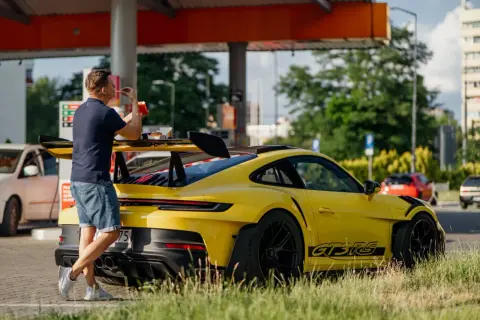 Żółty Porsche 911 GT3 RS z wielkim skrzydłem, obok którego stoi mężczyzna jedzący frytki.