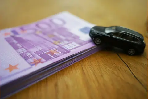 Czarny model samochodu na stosie banknotów 500 euro. Wartość rynkowa samochodu, tabela, urząd skarbowy - wszystko w jednym kadrze.