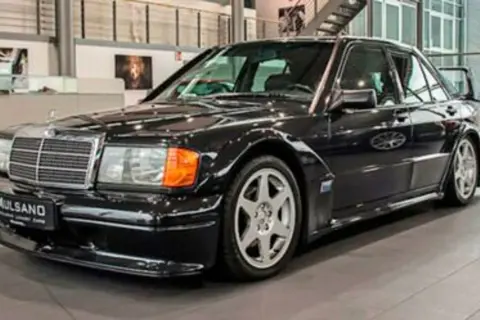 Czarny Mercedes 190 Evo z charakterystycznym spojlerem i felgami, stojący w salonie samochodowym.
