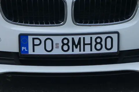 Białe auto z tablicą rejestracyjną PO 8MH80. W tle kratka grilla.