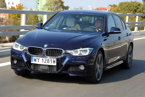 Ciemnoniebieskie BMW F30 M Pakiet pędzi po drodze. Kierowca skupiony na trasie.