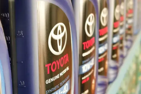Rząd butelek oryginalnego oleju Toyota. Kto produkuje? Toyota, znana marka samochodów, produkuje również wysokiej jakości oleje silnikowe.