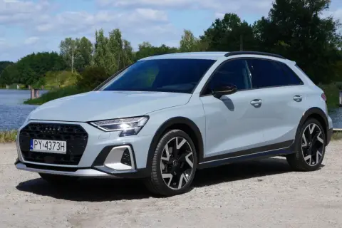 Jasnoszary Audi A3 allstreet stoi na żwirowej drodze nad jeziorem.