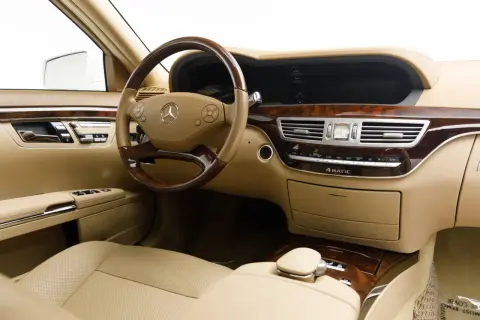Wnętrze luksusowego Mercedesa S 500 z beżową skórzaną tapicerką, drewnianymi wstawkami i kierownicą.