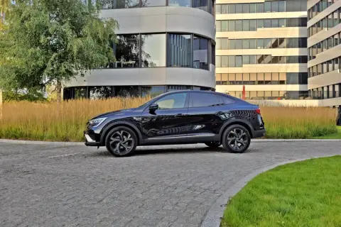 Elegancki, czarny Renault Arkana na tle nowoczesnych budynków biurowych.
