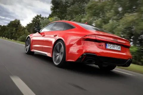 Czerwone Audi RS 7 pędzi po drodze, otoczone zielenią drzew.