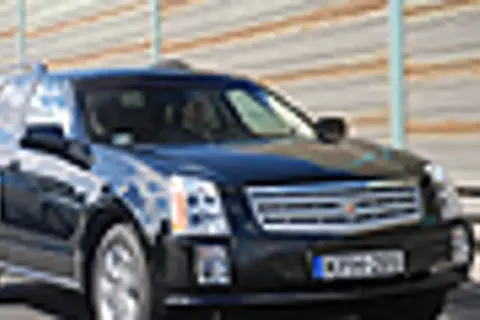 Czarny Cadillac SRX z przyciemnianymi szybami i chromowanymi detalami jedzie po drodze.